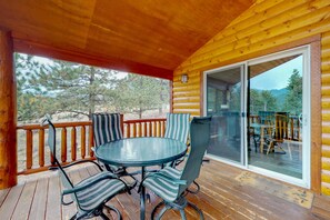 Eine Holzterrasse mit Glastür, die zu einem Außenbereich führt, umgeben von Kiefern.