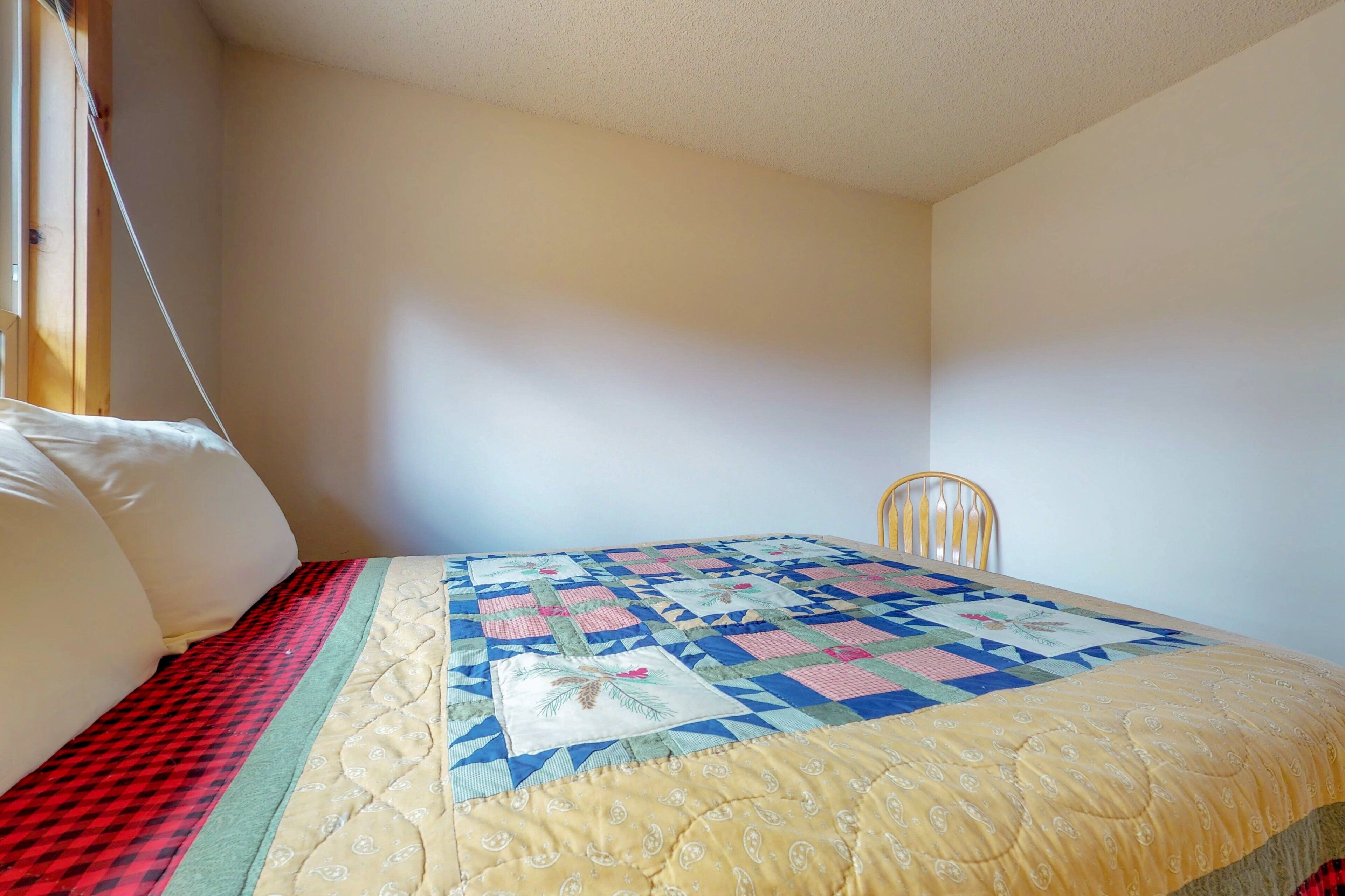 Un dormitorio con cama, una silla y un edredón.