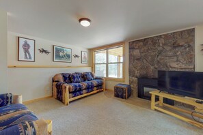A living room with a stone fireplace, a sofa, a television on a wooden stand, and framed pictures on the wall. - Wonderful Location With Full Kitchen, Furnished Deck & Mountain Views (Estes Park)