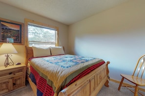 A bedroom with a wooden bed, a nightstand with a lamp, a chair, a window with blinds, and a framed picture on the wall. - Wonderful Location With Full Kitchen, Furnished Deck & Mountain Views (Estes Park)