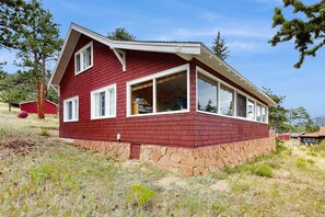 Ein rotes Holzhaus mit Steinunterbau, großen Fenstern und einem geneigten Dach.