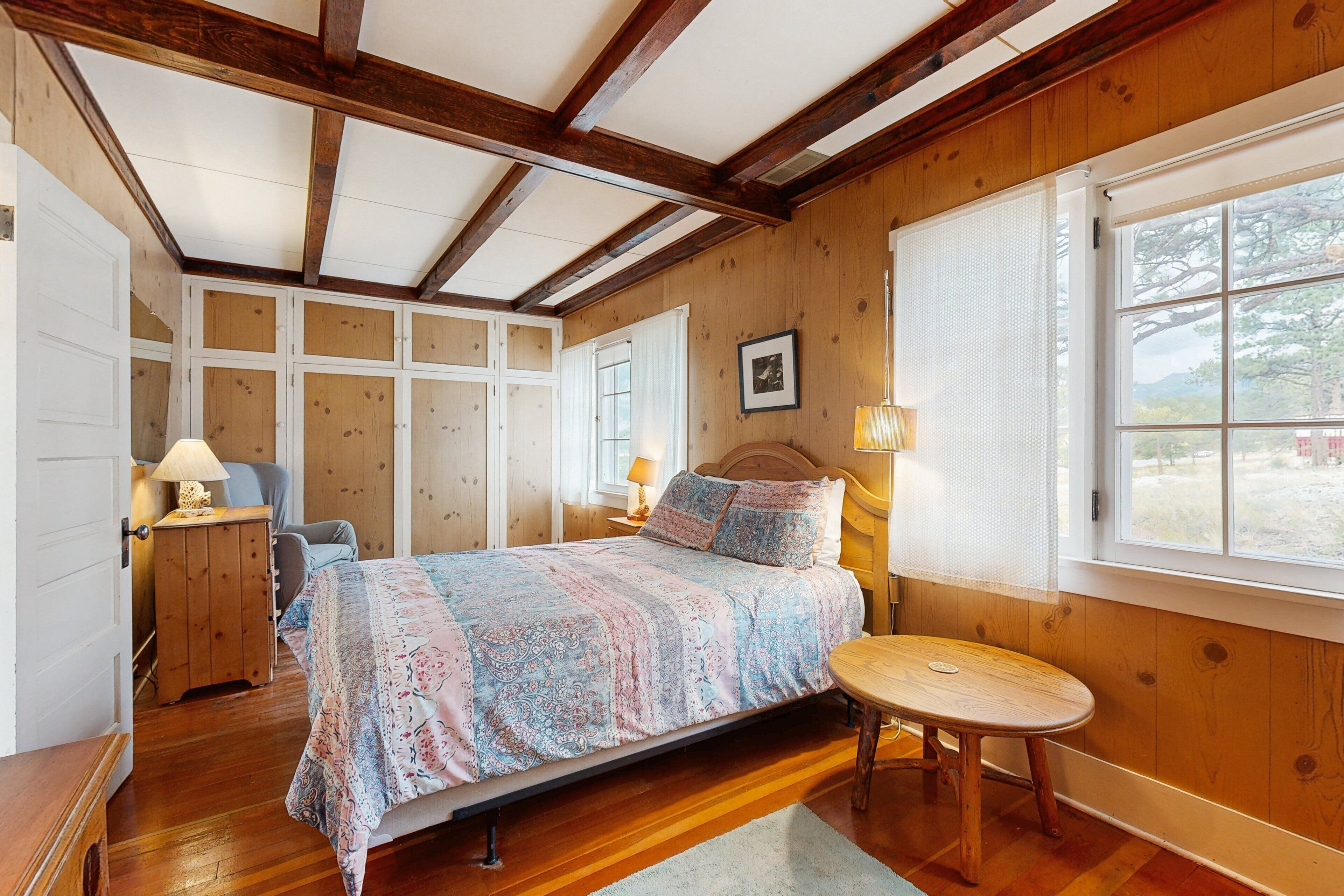 Een slaapkamer met een bed, nachtkastje, stoel, raam en houten wanden.