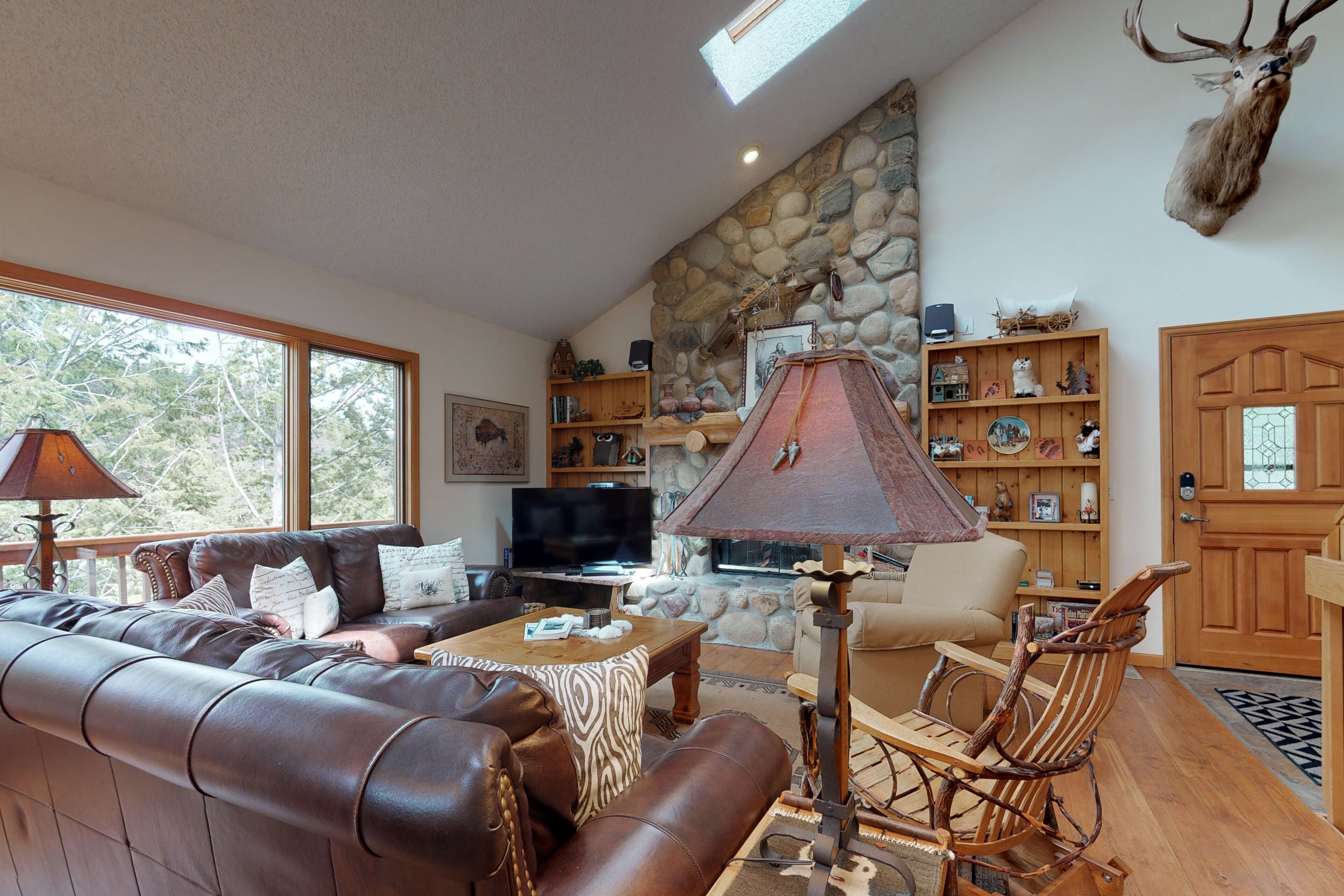 A cozy living room with leather sofas, a stone fireplace, and a mounted deer head.