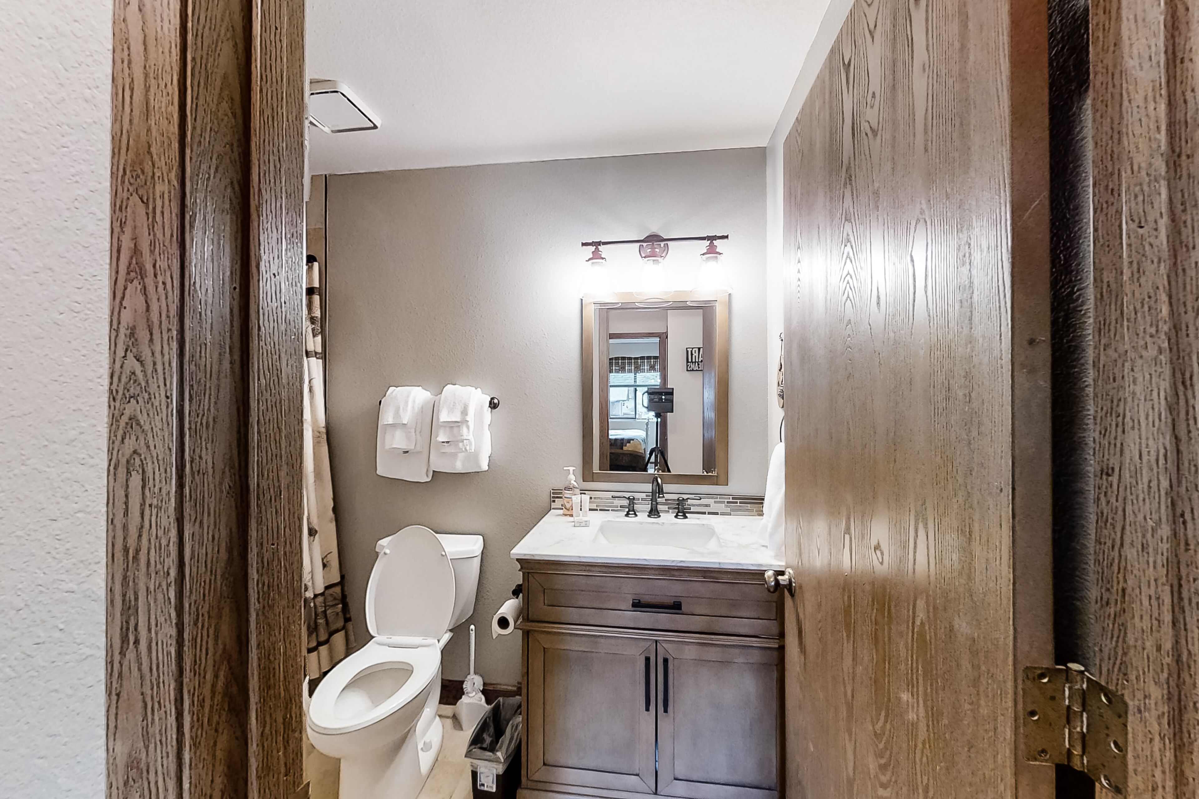 A bathroom with a toilet, sink, vanity, and mirror.