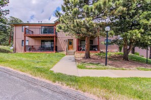 A two-story building with a balcony, a front door, and a sidewalk leading to the entrance. - Conveniently Located Mountain Condo With Balcony, Wildlife Views, & Golf Course (Estes Park)