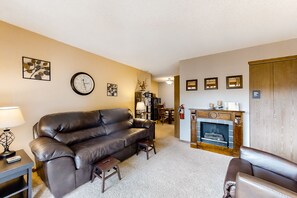 Ein Wohnzimmer mit braunem Ledersofa, einem kleinen Tisch mit Lampe, einem Kamin und einer Treppe, die in einen anderen Raum führt.