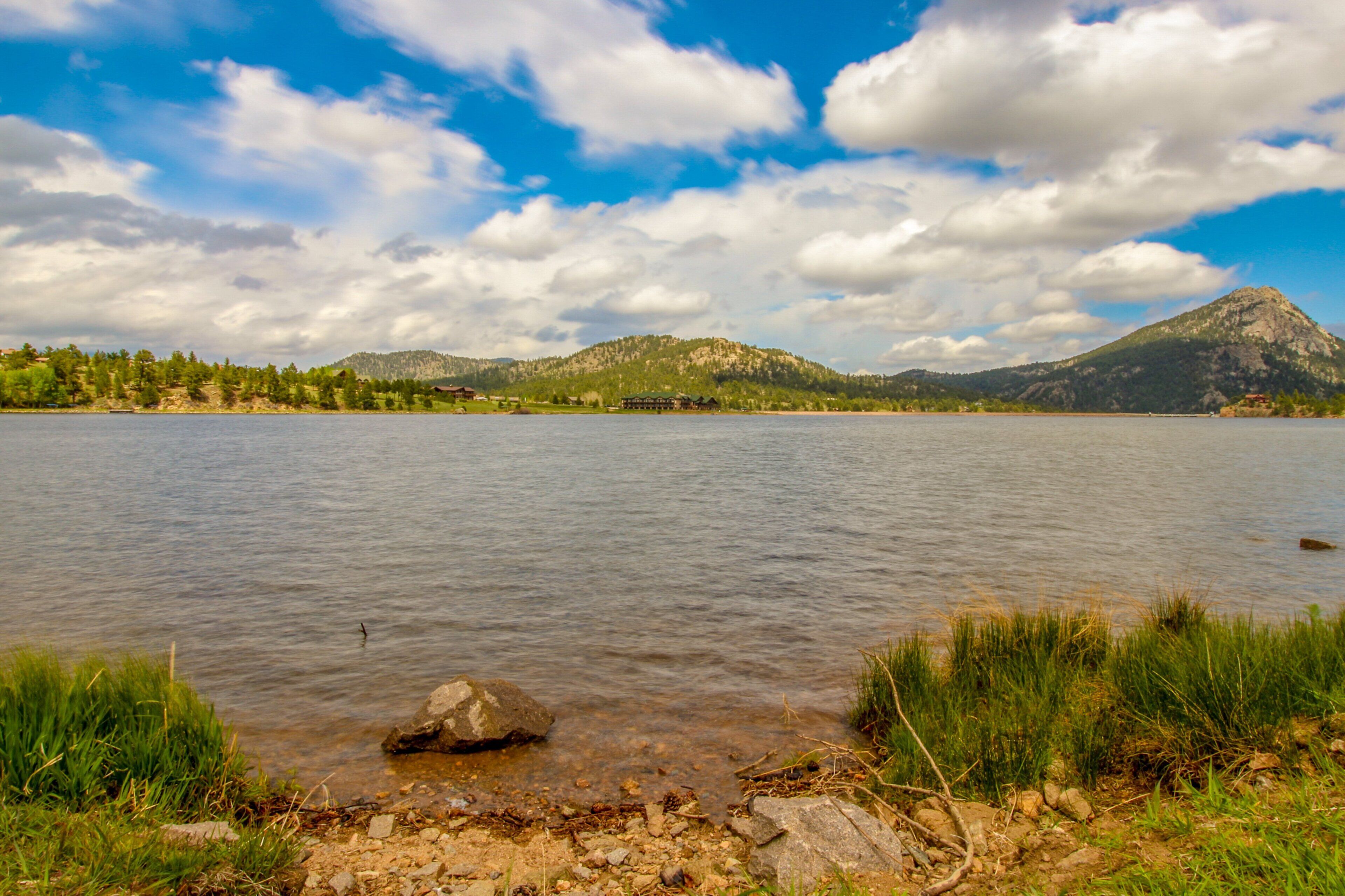 Un lago con una montaña al fondo, cielos despejados y un edificio pequeño en la orilla.
