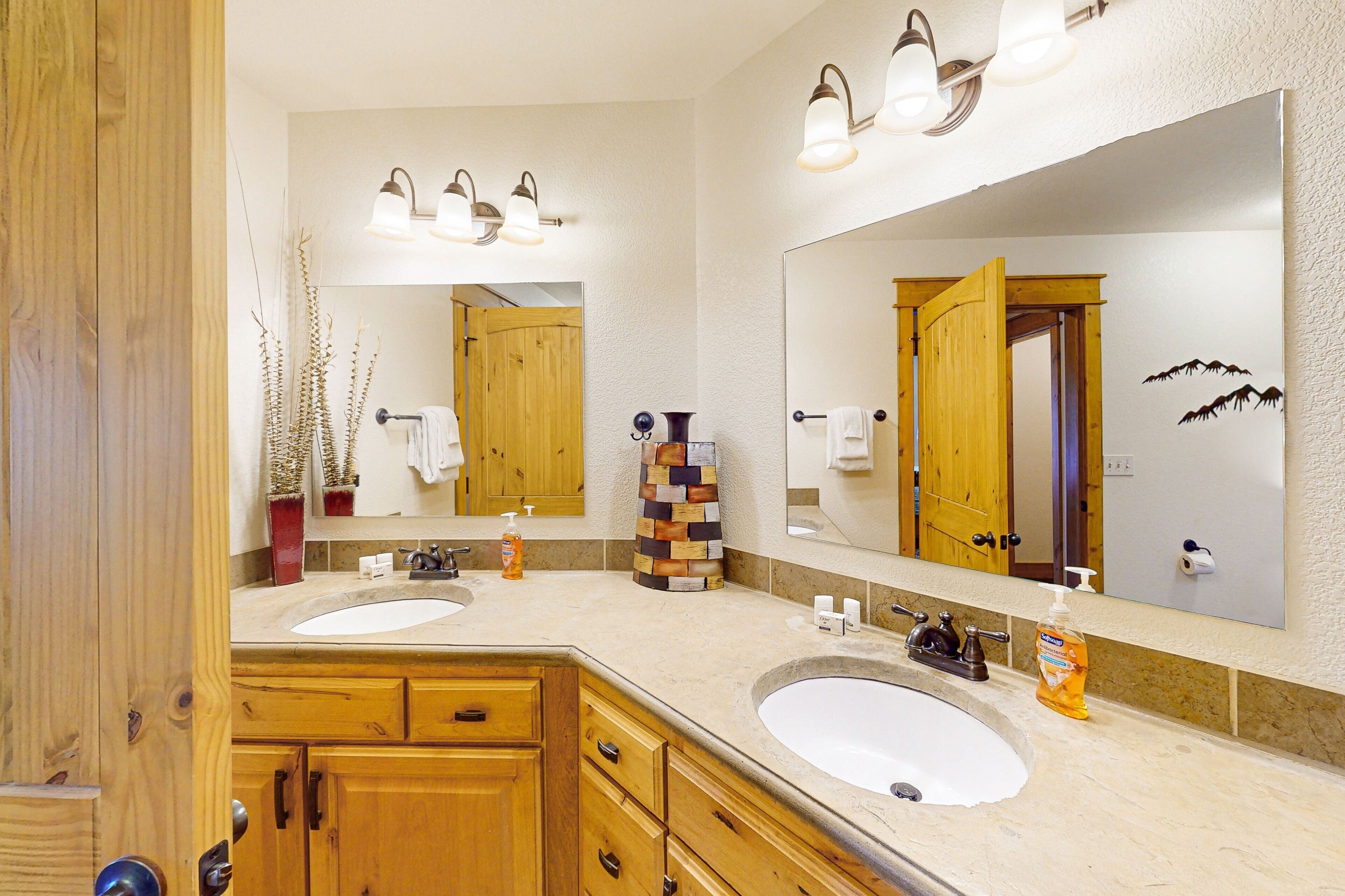 A bathroom with two sinks, wooden cabinets, a large mirror, and a decorative vase.