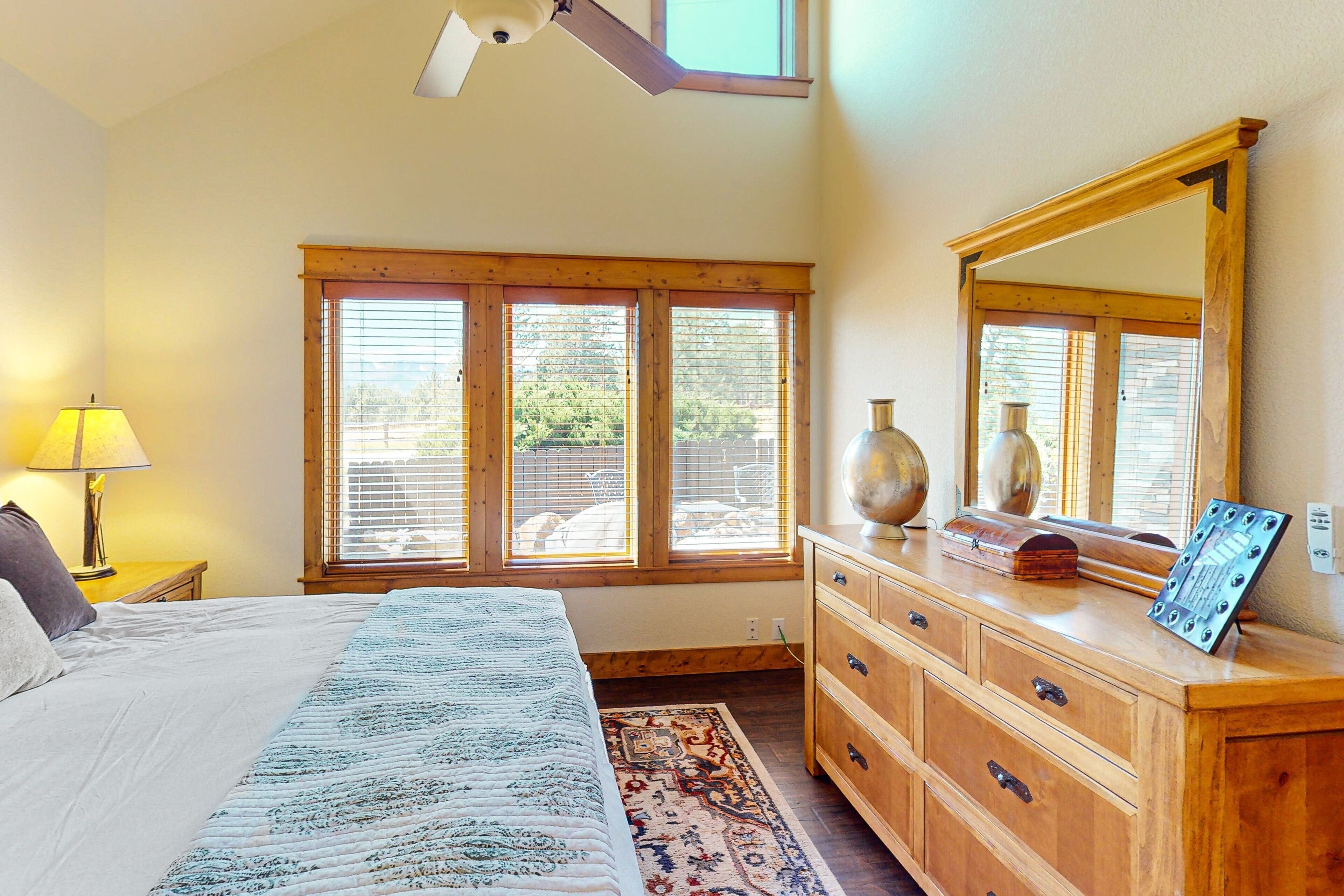 A bedroom with a bed, wooden dresser, large mirror, and a window with blinds.