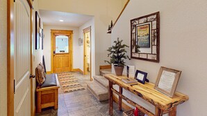 A hallway with a bench, a small Christmas tree, a wooden table with a framed sign, and a door. - Luxurious Dog-friendly Townhome Near Lake Estes With Fantastic Views (Estes Park)