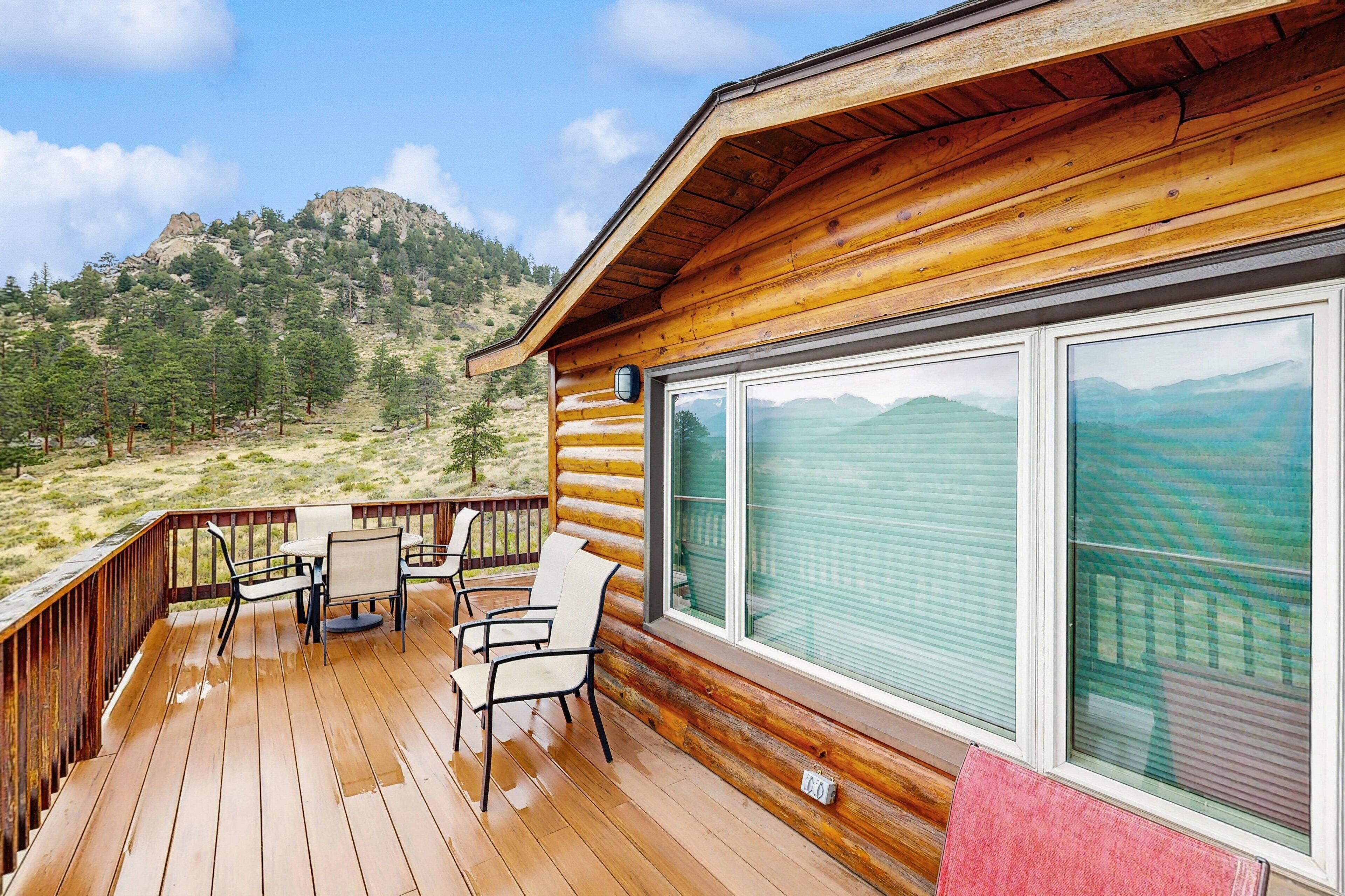 A wooden deck with outdoor furniture, a large window, and a mountainous landscape view.