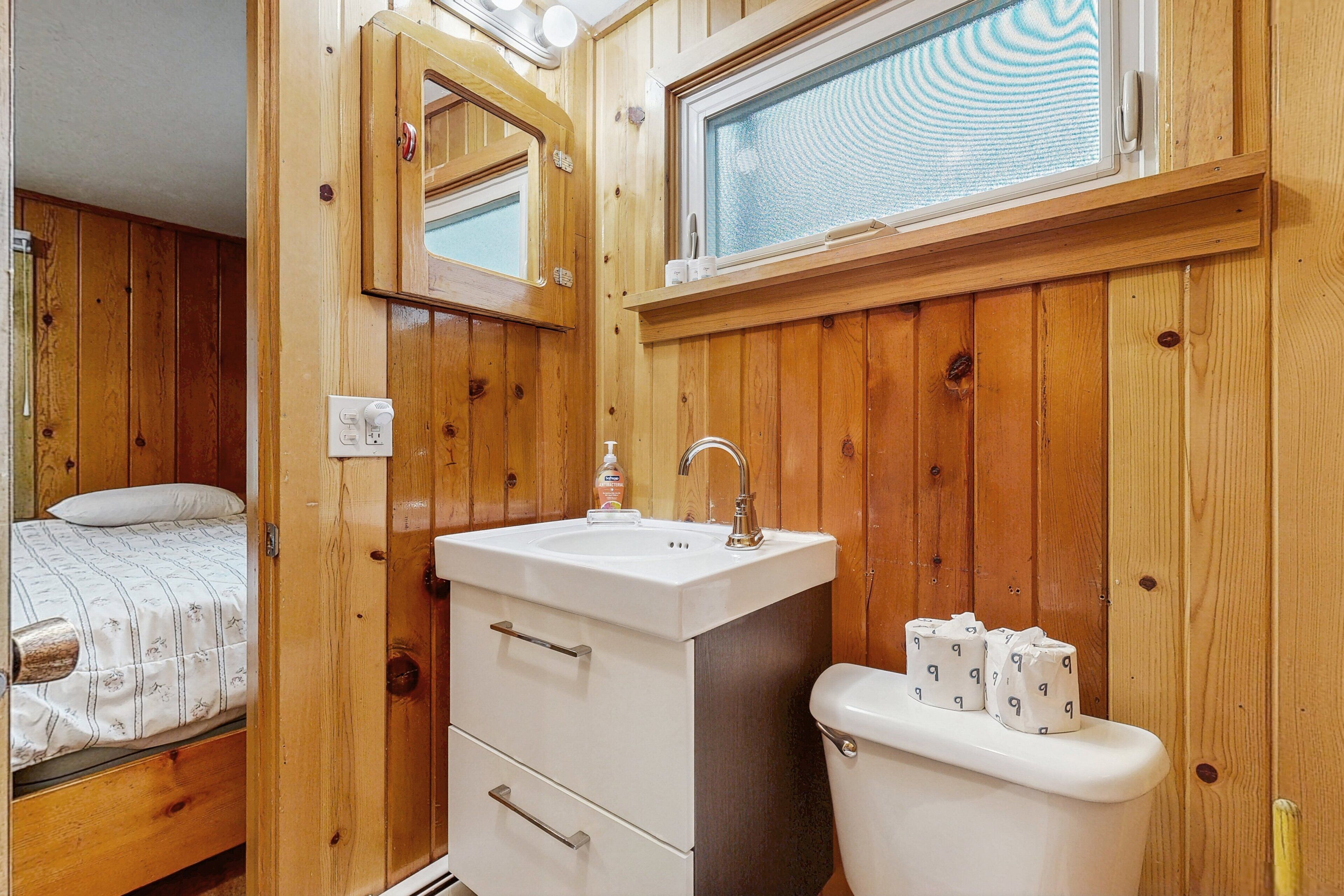 A wooden-paneled bathroom with a sink, mirror, and toilet.