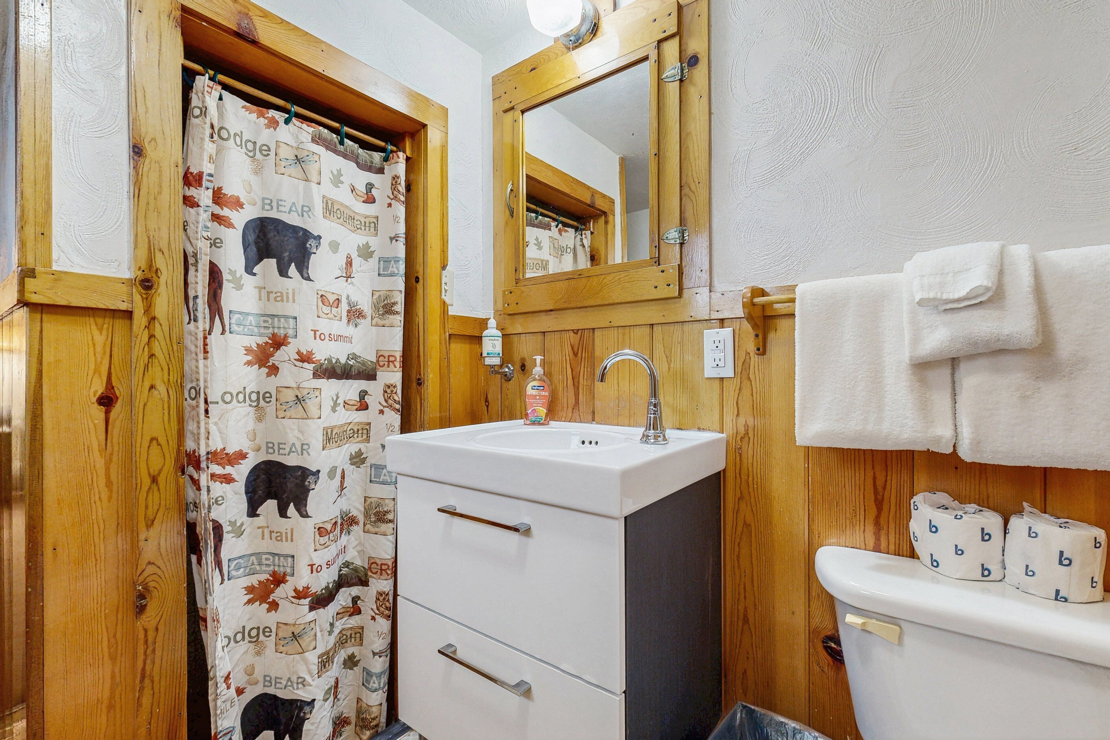 A bathroom with a wooden door, a white sink, a mirror, and a toilet with a towel hanging on the wall.