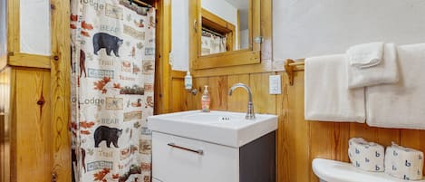 A bathroom with a wooden door, a white sink, a mirror, and a toilet with a towel hanging on the wall.