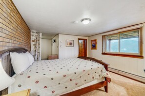 Ein Schlafzimmer mit einem hölzernen Bett, einem Fenster mit Blick auf die Berge, einer Ziegelwand und einer weißen Decke.