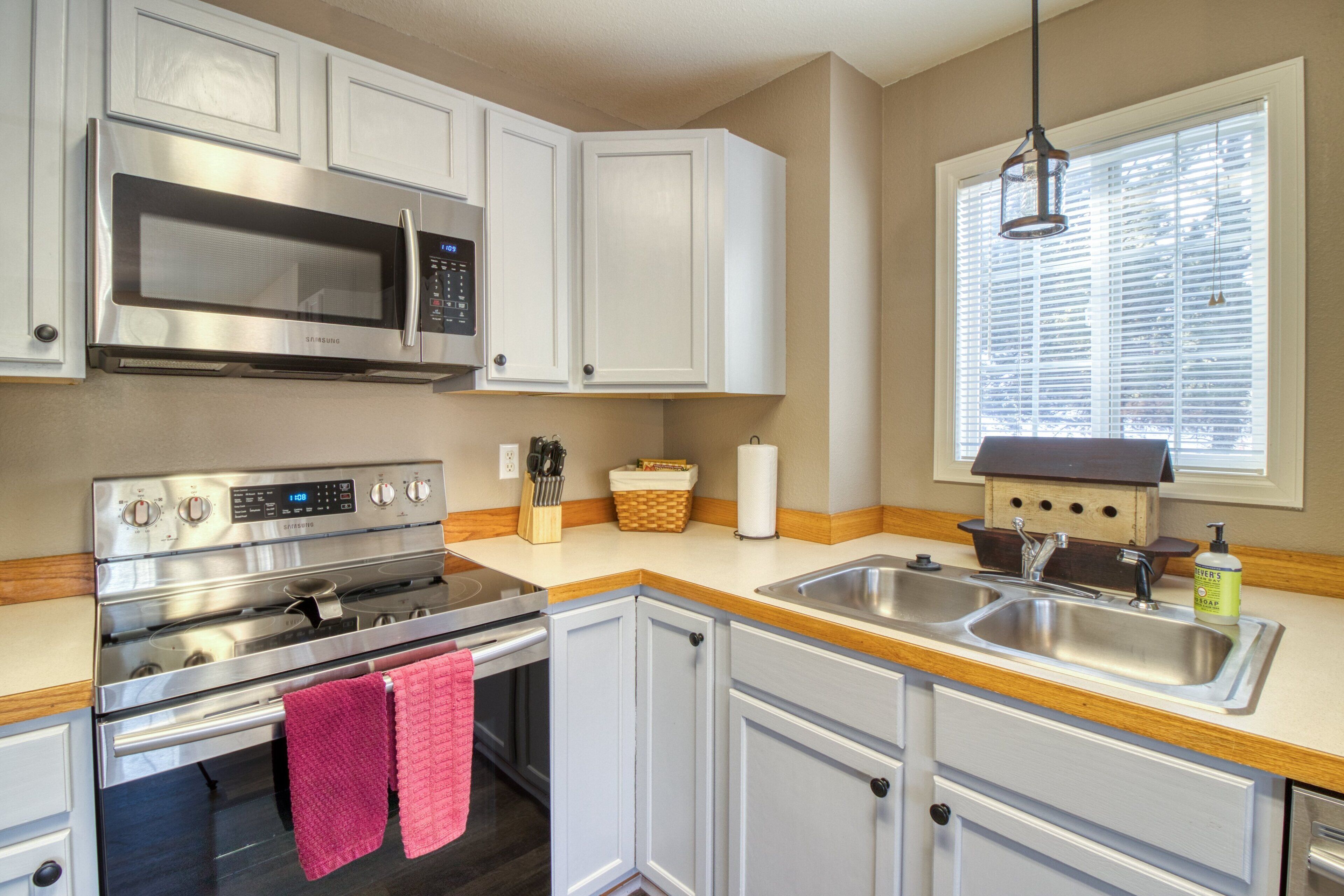 A kitchen with white cabinets, stainless steel appliances, a wooden countertop, and a window with blinds.