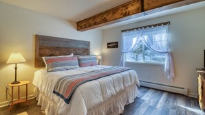 Een slaapkamer met een houten hoofdbord, een groot bed met veel kussens, een bedlampje, een raam met gordijnen en een radiator.