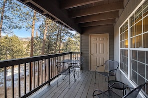 A covered porch with a wooden deck, metal chairs, and a door. - Relaxing Condo in Estes Park w/ a Full Kitchen, gas Fireplace, & Furnished Deck (Estes Park)