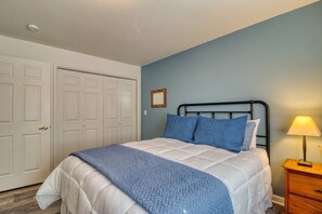 Quarto com cama, mesa de cabeceira, luminária e porta.