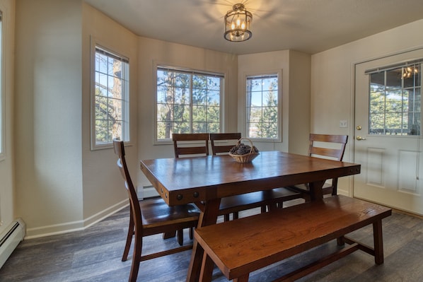 Uma sala de jantar com uma mesa de madeira, quatro cadeiras, um banco e uma cesta sobre a mesa.