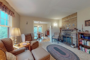A cozy living room with a fireplace, a bookshelf, and a dining area with a table and chairs. - Secluded Vacation Home With Lake & Mountain Views - Walk to Downtown (Estes Park)