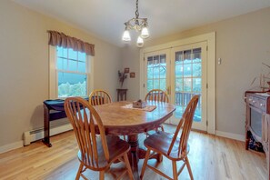 A dining area with a round wooden table, four chairs, a chandelier, and a view through the window. - Secluded Vacation Home With Lake & Mountain Views - Walk to Downtown (Estes Park)
