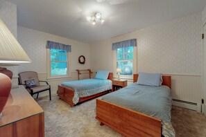 Ein Schlafzimmer mit zwei Betten, einem Sessel, einem Schreibtisch und einer Lampe.