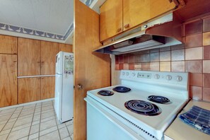 Eine Küche mit Holzschränken, einem weißen Kühlschrank und einem weißen Herd mit vier Kochfeldern.