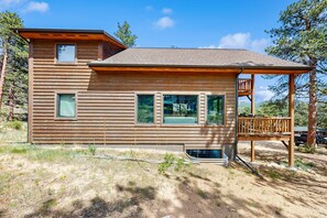 Eine Holzblockhütte mit einer Terrasse, großen Fenstern und einem kleinen Balkon im Obergeschoss.