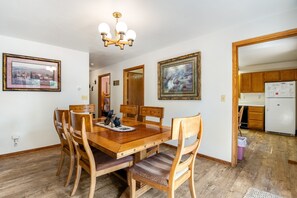Un comedor con una mesa y sillas de madera, una araña y cuadros en las paredes.