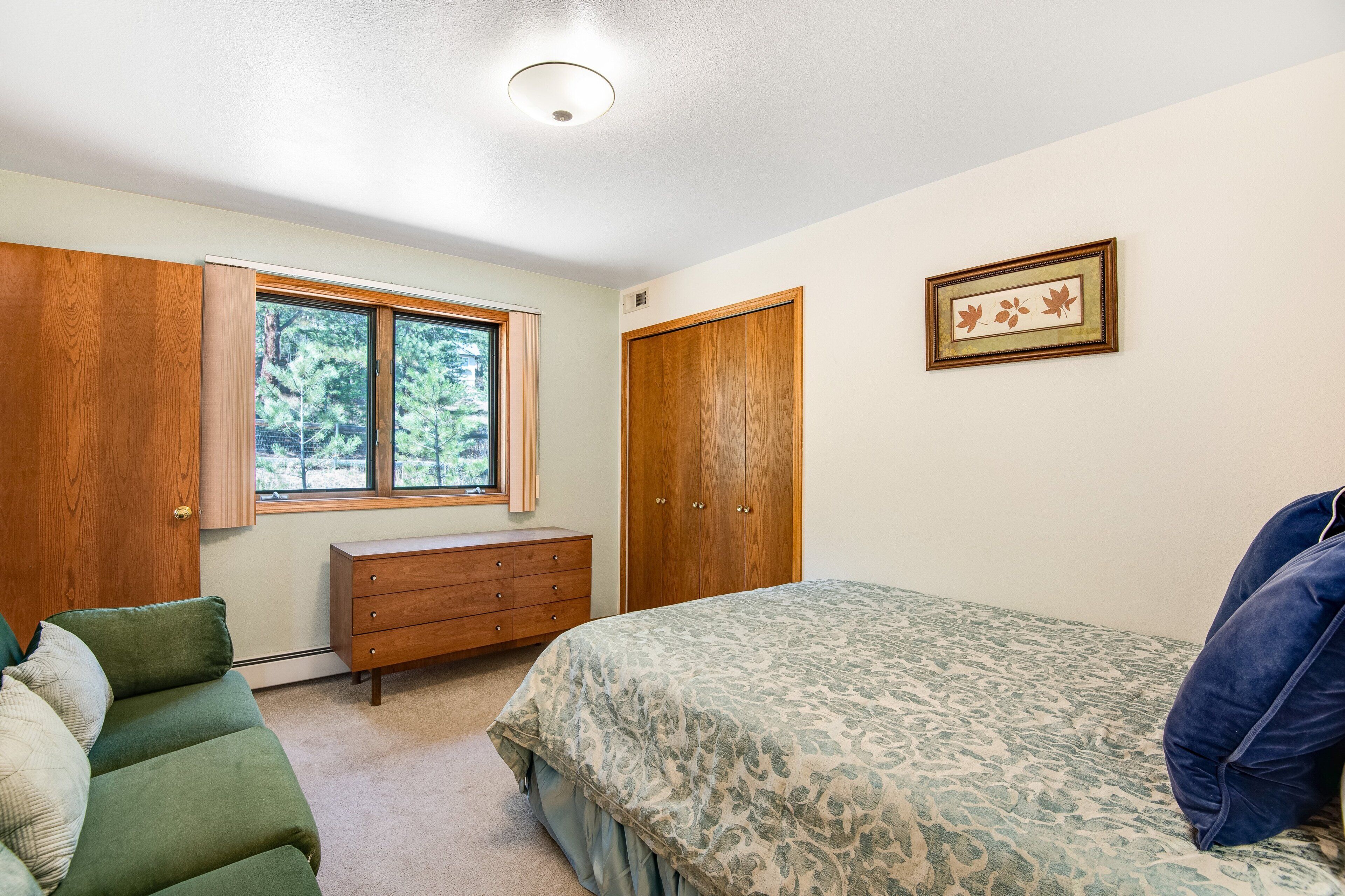 A bedroom with a bed, dresser, and wardrobe, a window with a view of trees, and a framed picture on the wall.