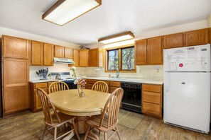 Una cocina con armarios de madera, un refrigerador blanco, una mesa de comedor con sillas y una ventana.
