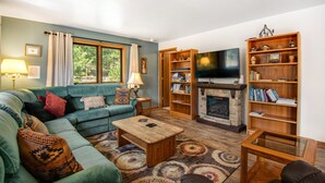 A living room with a sofa, coffee table, fireplace, bookshelf, and television. - Dog-friendly, Mountain-view Home With Deck & Grill (Estes Park)