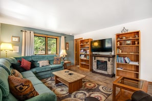 Una sala de estar con sofá, mesa de centro, chimenea, estantería y televisor.
