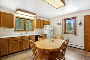 Una cocina con armarios de madera, una encimera blanca, un refrigerador y una mesa de comedor con sillas.