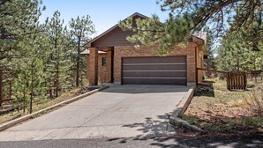 A two-story brick house with a garage, surrounded by pine trees. - Dog-friendly, Mountain-view Home With Deck & Grill (Estes Park)