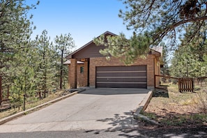 A two-story brick house with a garage, surrounded by pine trees. - Dog-friendly, Mountain-view Home With Deck & Grill (Estes Park)