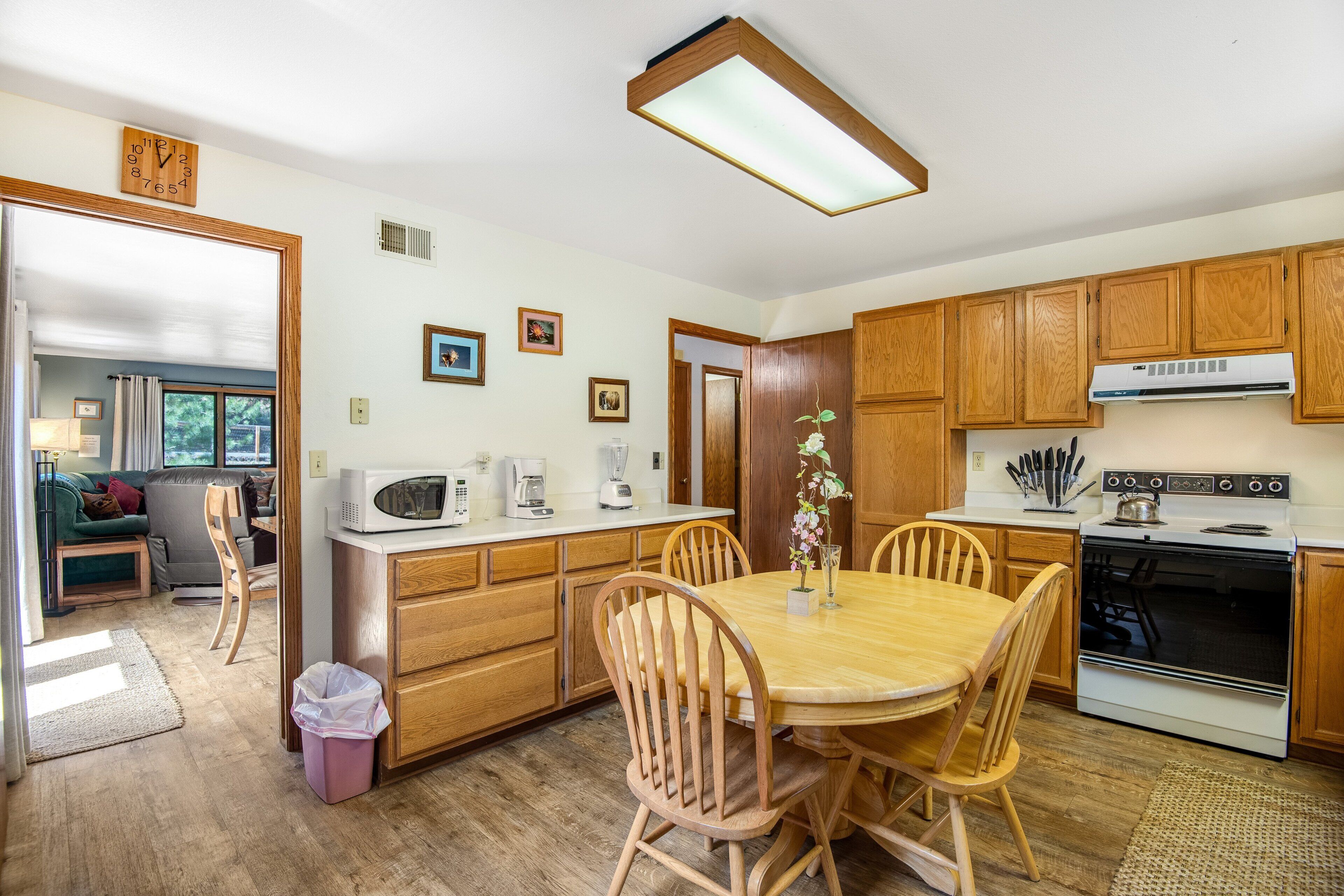 A kitchen with wooden cabinets, a dining table with chairs, a microwave, a stove, and a trash can.