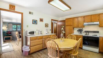 A kitchen with wooden cabinets, a dining table with chairs, a microwave, a stove, and a trash can.