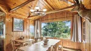 Ein Holzinterieur mit Esstisch, Stühlen, einer Kronleuchter und einem aufgehängten Tierkopf.