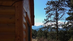 Eine Holzdiele mit Blick auf eine Kiefer und Berge im Hintergrund.