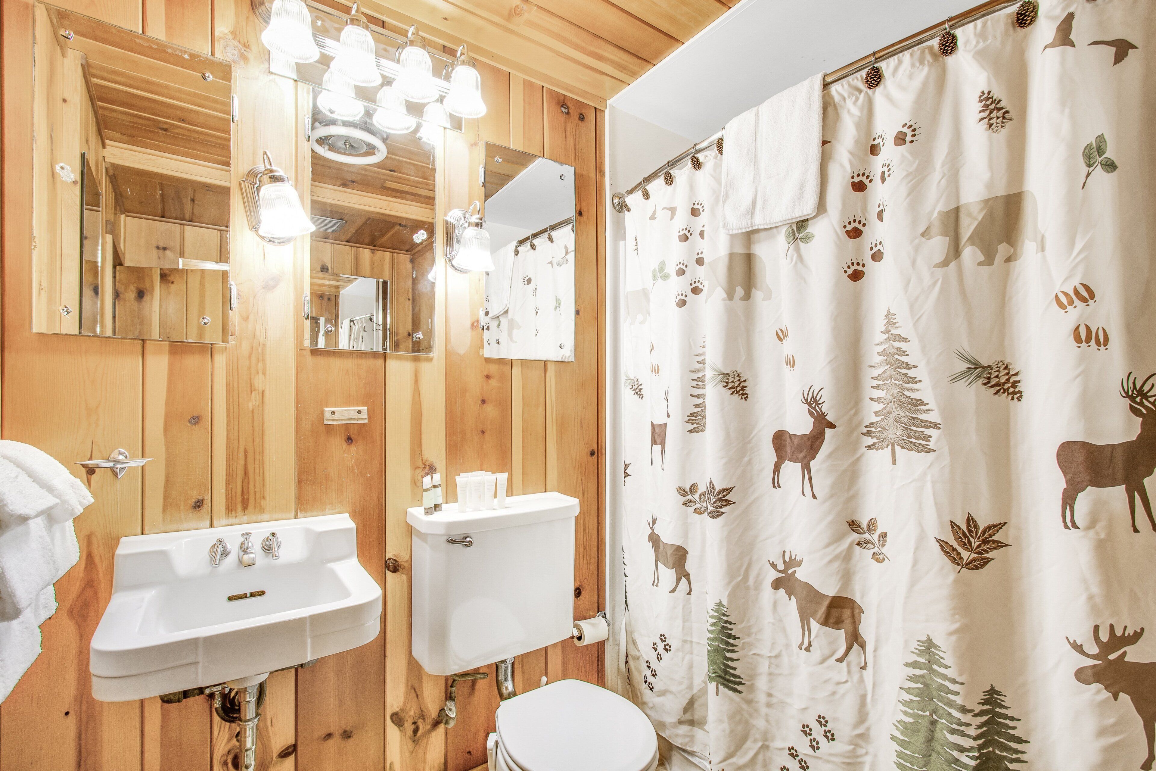 A wooden bathroom with a sink, mirror, and toilet.