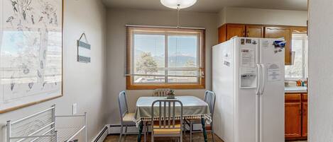 A compact kitchen with a dining table, chairs, a refrigerator, and a window with blinds.