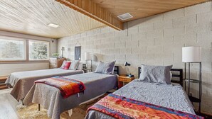 Una habitación con dos camas, techo de madera, paredes de ladrillo, lámparas de noche y una ventana con persianas.