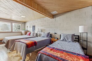 Ein Zimmer mit zwei Betten, Holzboden, Backsteinwänden, Nachttischlampen und einem Fenster mit Jalousien.