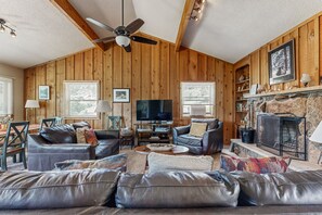 Una sala de estar acogedora con paredes de madera, una chimenea, sofás de cuero y un televisor.