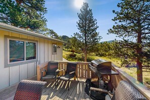 Eine Terrasse mit Gartenmöbeln, einem Grill und Blick auf einen bewaldeten Bereich.