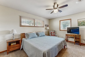 Ein Schlafzimmer mit Bett, Nachttisch, Lampe, Fernsehschrank, Deckenventilator und zwei Fenstern.