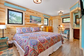 Una cabaña de madera con una cama grande, dos ventanas, un cuadro y una televisión.