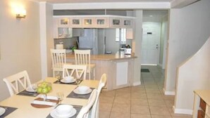 Een eetgedeelte met een tafel gedekt voor vier personen, een keuken op de achtergrond en een trap naar een hoger niveau.
